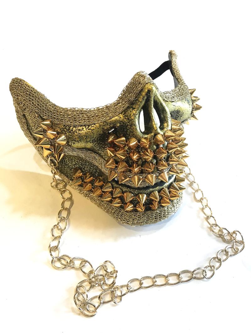 A textured mask with gold studs and spikes, featuring a chain across the front. The design is edgy and bold, with metallic accents giving it a rugged, dramatic appearance.