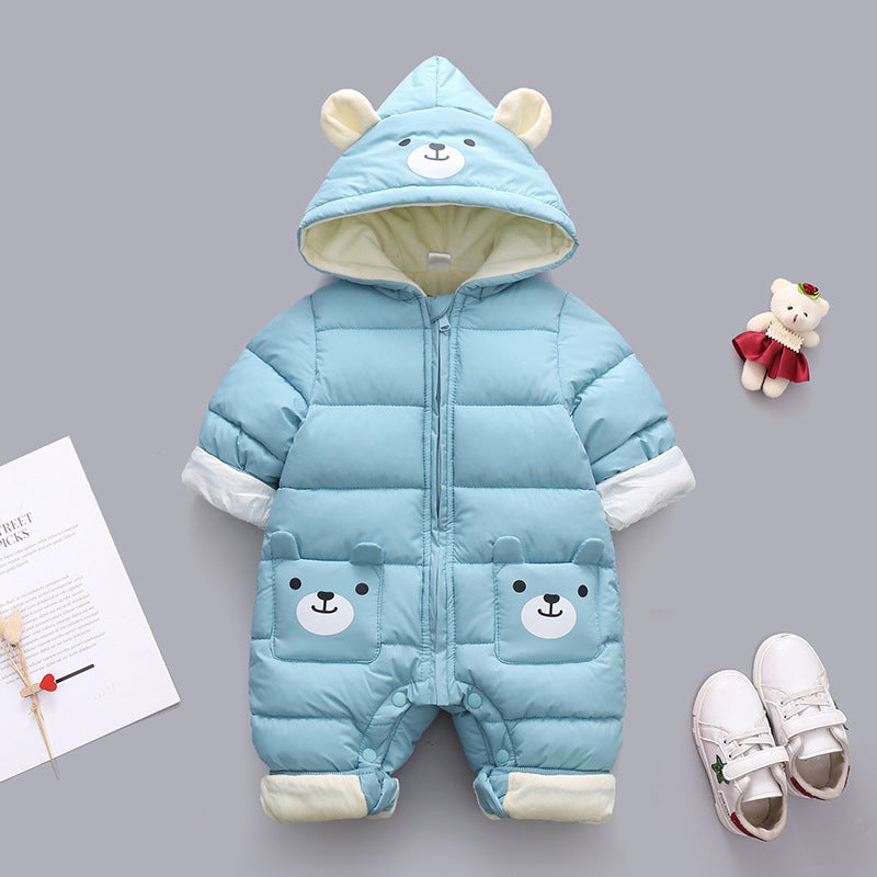 Blue baby onesie with bear ears and face on the hood, bear face pockets, with white sneakers, a small toy teddy in a dress, and a paper with a heart decoration nearby.
