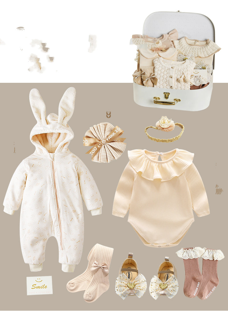 Baby clothing set includes a bunny-eared onesie, frilly bodysuit, headband, ribbon, socks, bow shoes, and a suitcase filled with pastel outfits, shoes, and accessories.