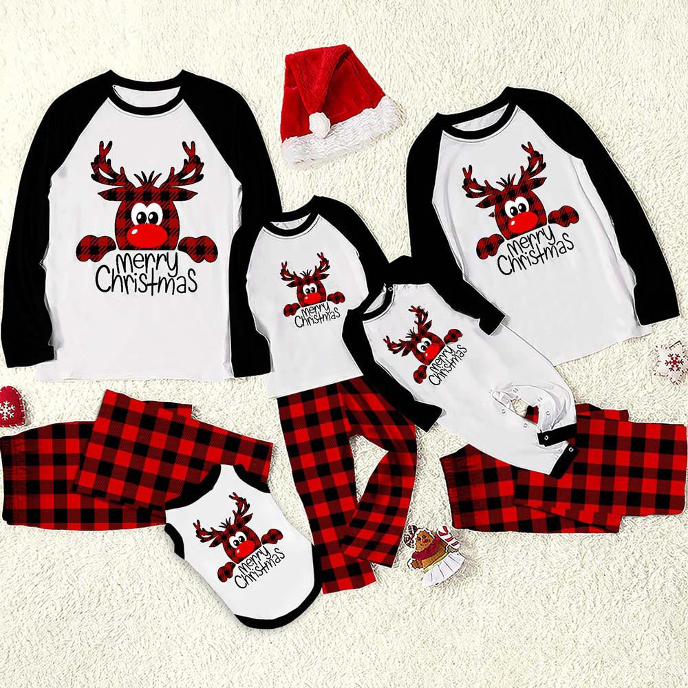 Matching Christmas pajamas for a family, featuring a red plaid reindeer design. Includes tops with "Merry Christmas" and plaid pants. A Santa hat lies nearby on a fluffy surface.