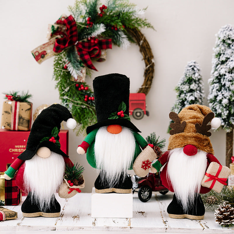 Three plush Christmas gnomes with hats, holding holiday decorations and gifts, stand before a festive background of wreaths, trees, and wrapped presents on a wooden table.