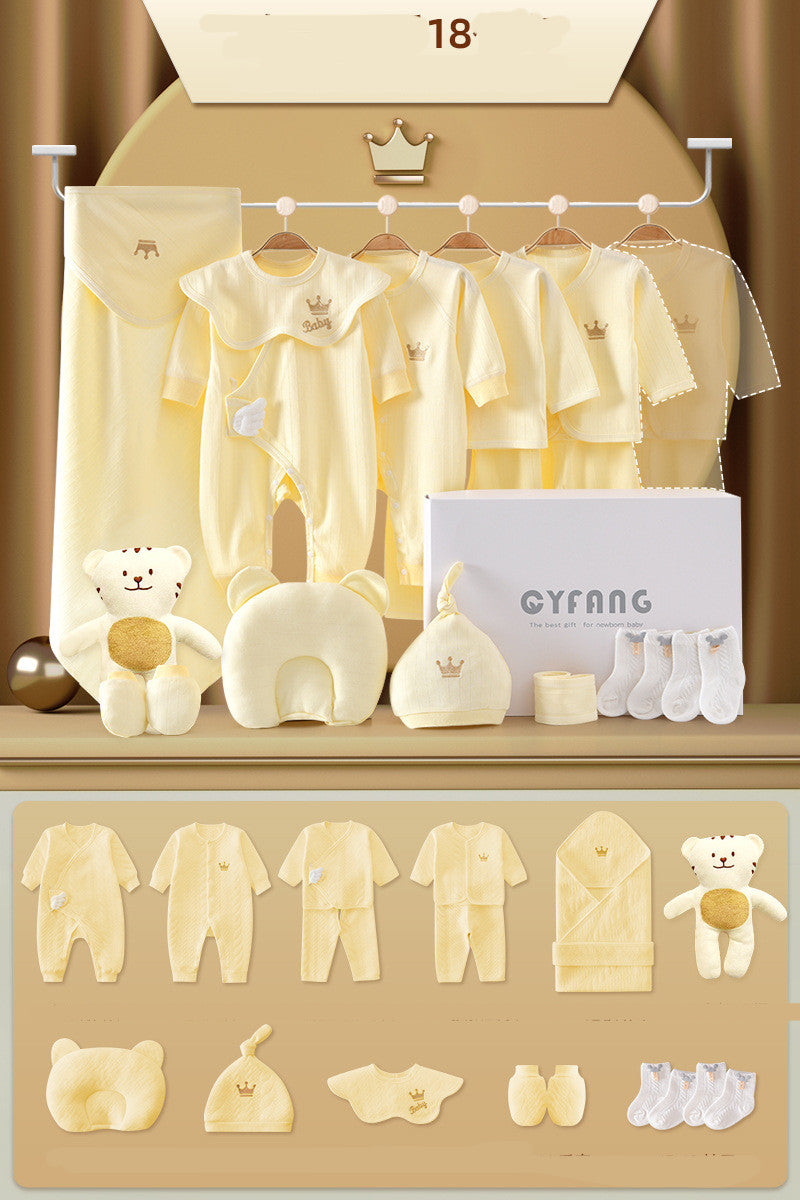 Baby gift set includes yellow clothing like onesies and mittens, a blanket, socks, hat, plush bear, and pillow, all with crown motifs, displayed neatly in bright lighting.