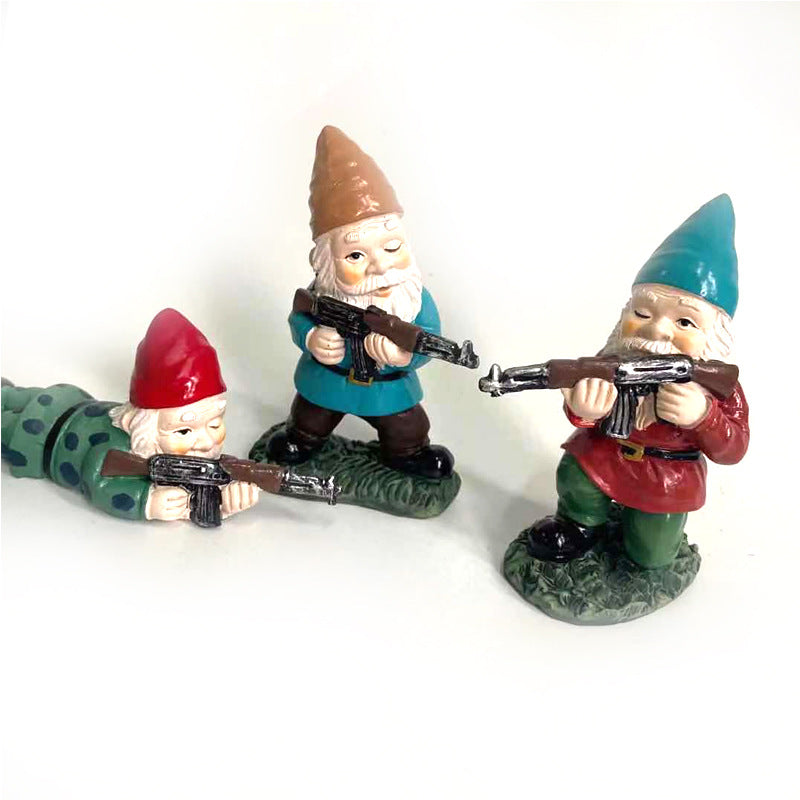 Three garden gnomes, each holding a rifle. One is lying prone in green, while the others stand in blue and red outfits. They have cheerful expressions and point forward.