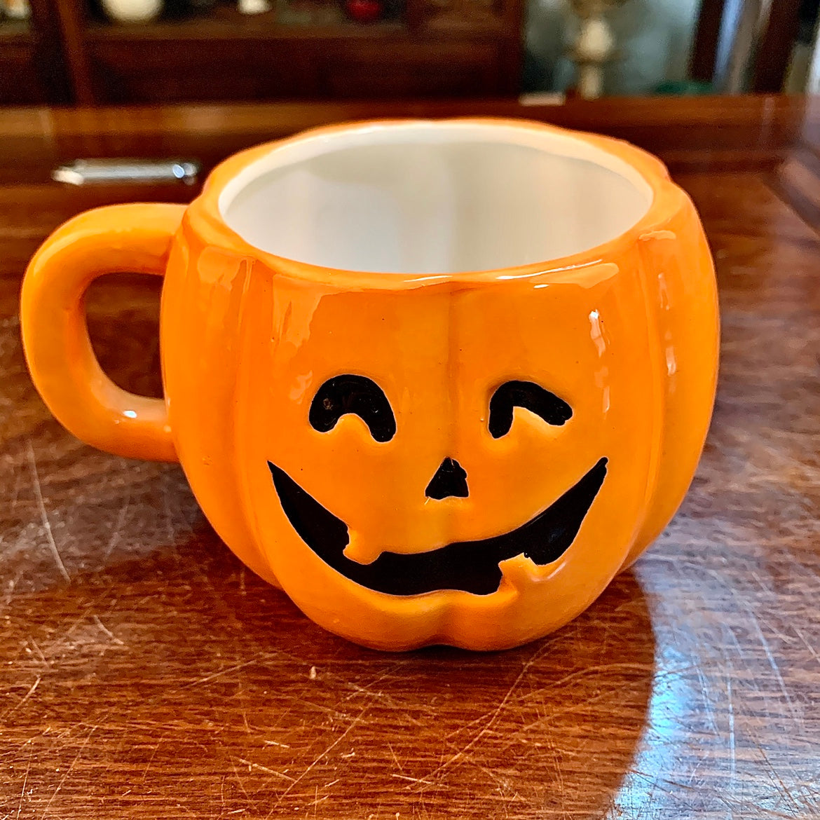 Orange pumpkin-shaped mug with a carved, smiling jack-o'-lantern face, placed on a wooden surface.