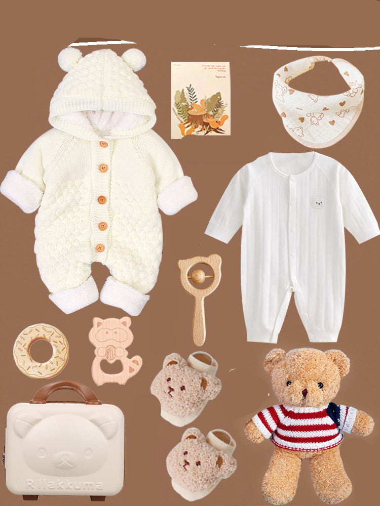 Assorted baby items on a brown background, including a knit onesie with bear ears, a white romper, bib, toys, bear mittens and briefcase, and a striped teddy bear.