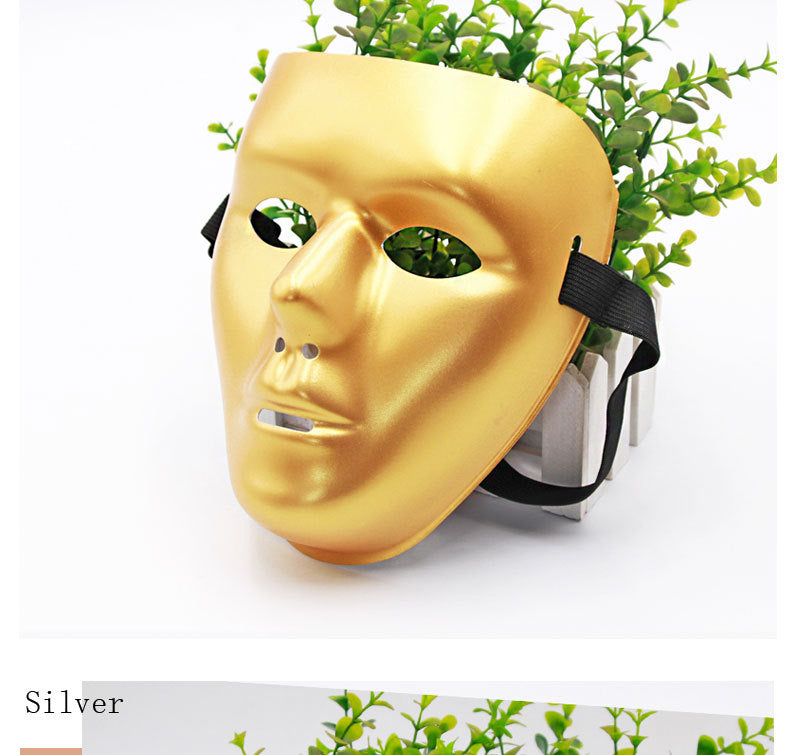 A gold mask with black straps rests against a small planter with green leaves peeking through the eye holes and mouth opening, all set on a white background.