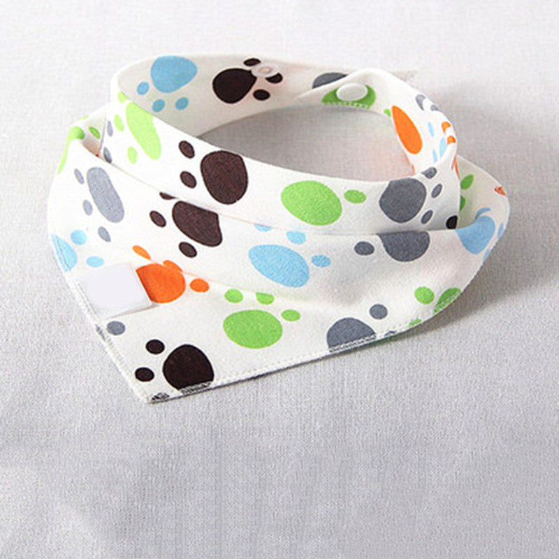 A white baby bandana bib with colorful paw prints in blue, green, orange, gray, and black, secured with a snap button, laid flat on a light gray surface.