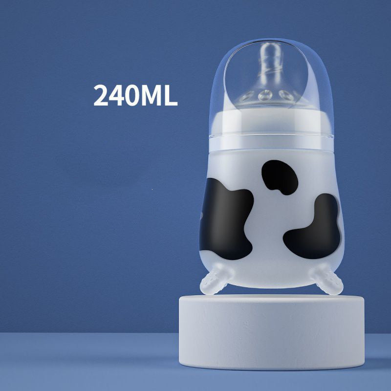 Baby bottle with a cow pattern design on a blue background, labeled 240ML. The bottle is placed on a white cylindrical stand and has a clear cap.