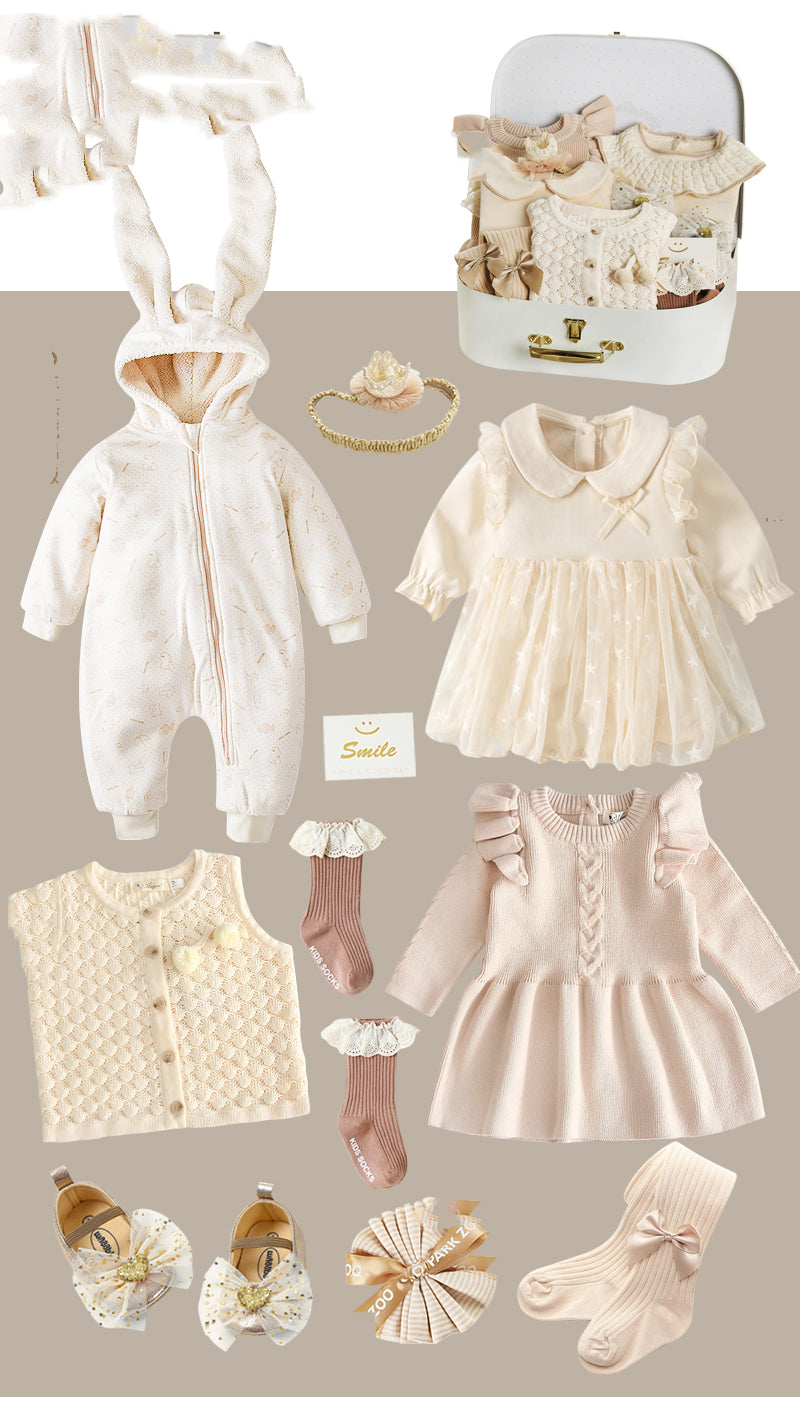 A collection of pastel baby clothes, including a bunny onesie, lace dress, knit sweater, socks, shoes, and a headband, arranged with a small suitcase labeled "Smile."