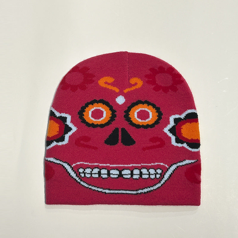 Red beanie with a vibrant Day of the Dead sugar skull design, featuring colorful patterns including orange and yellow eyes, a floral motif, and a toothy grin.