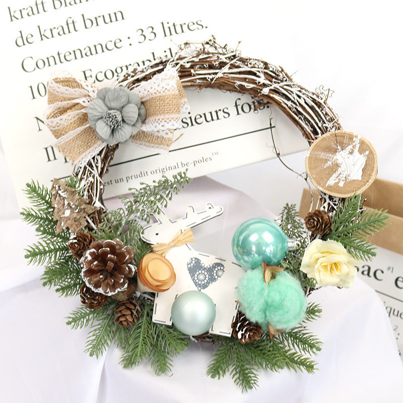 Festive wreath with pinecones, green ornaments, cotton, wooden disks, a reindeer cutout, and a large bow, surrounded by green foliage. Background has printed text.