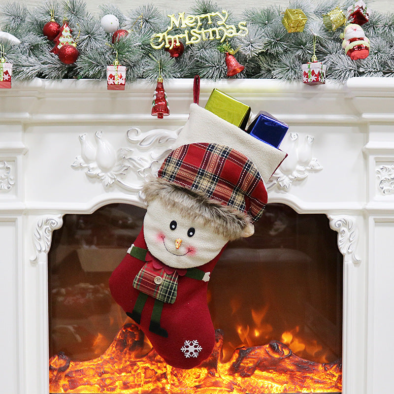 Festive Christmas stocking with a smiling plush face hangs on a white mantel adorned with garland, ornaments, and "Merry Christmas" sign above a glowing fireplace.