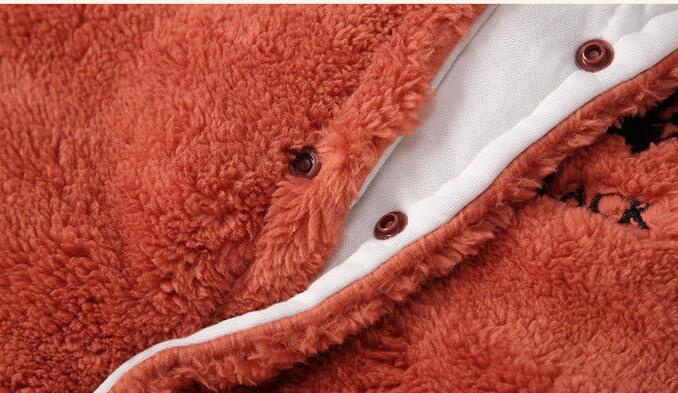 Close-up of a rust-colored, fluffy fabric with a white interior lining and snap buttons. The texture appears soft and warm, suitable for cozy clothing or blankets.