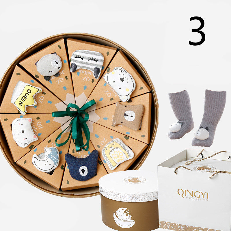 Round gift box with triangular compartments, each featuring animal-themed socks. A pair of gray socks is displayed separately. Includes a branded paper bag and a brown box with a white lid.