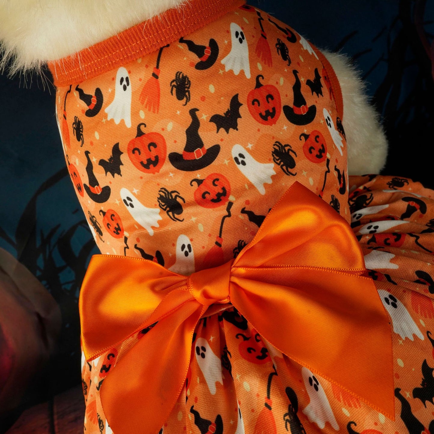 An orange dog outfit with Halloween-themed print, featuring ghosts, pumpkins, bats, and witch hats, topped with a large satin bow on the back.