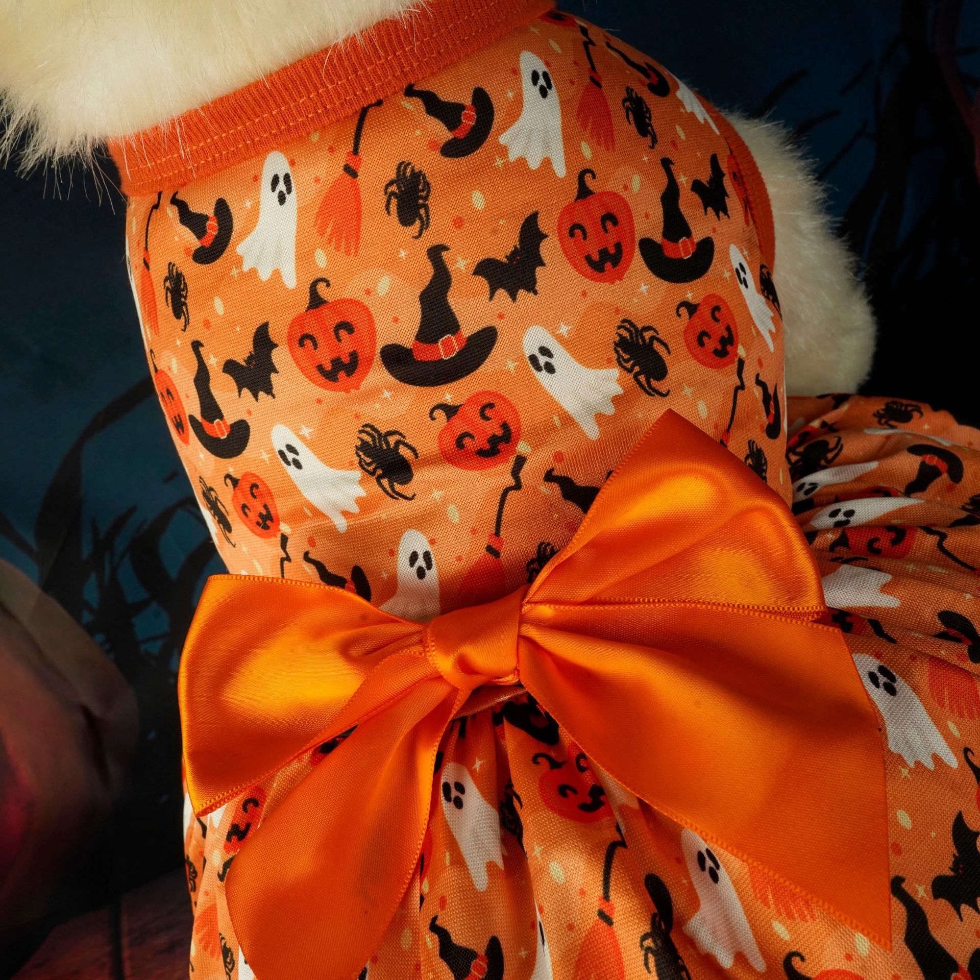 An orange dog outfit with Halloween-themed print, featuring ghosts, pumpkins, bats, and witch hats, topped with a large satin bow on the back.