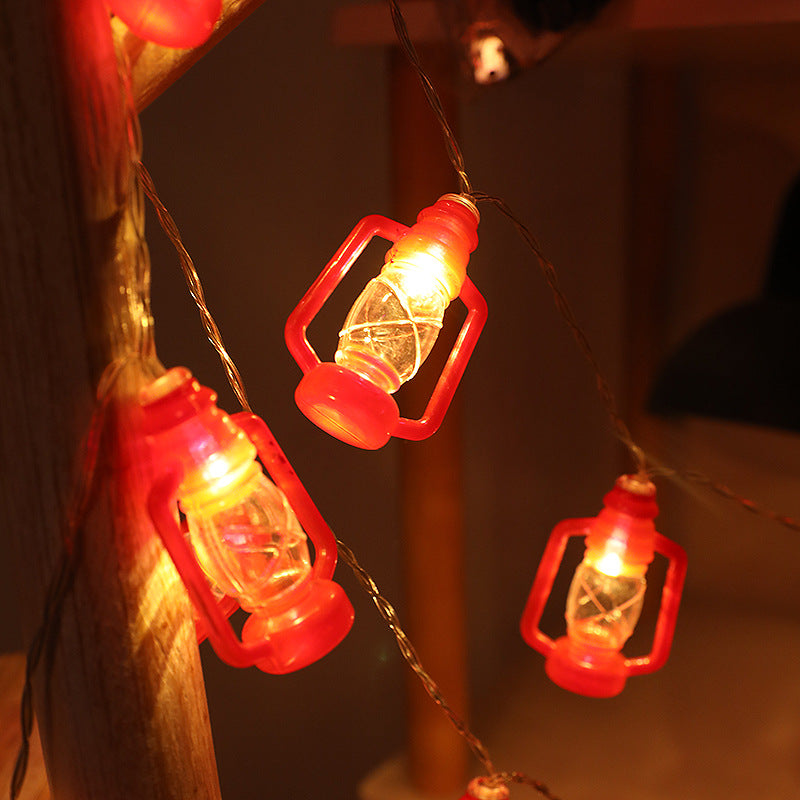 String lights shaped like small red lanterns glow warmly in dim surroundings, creating a cozy ambiance. The lanterns hang from a wire, casting soft shadows.