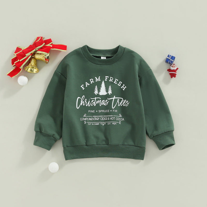 Green sweatshirt with "Farm Fresh Christmas Trees" printed in white. Nearby, gold bells with a red ribbon and small festive decorations are displayed.