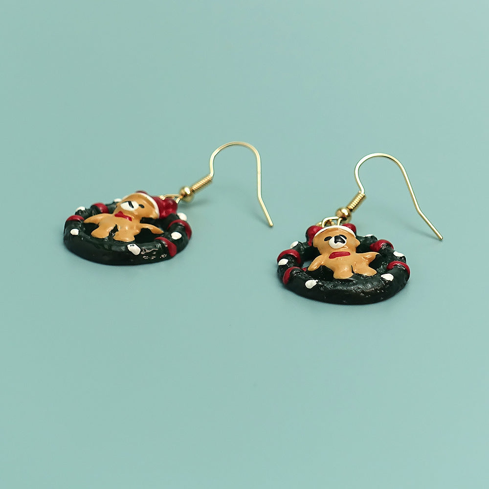 Festive earrings featuring gingerbread men on a black and red wreath, with gold hooks, set against a light green background. Perfect for holiday-themed accessories.