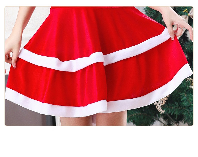 A person holds the edges of a festive red skirt with white trim, resembling a Santa costume, standing near a Christmas tree.