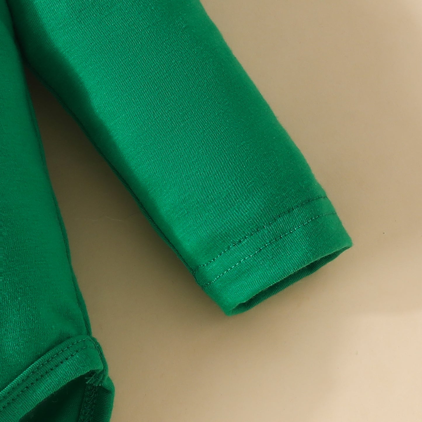 Close-up of a long green sleeve cuff, showing detailed stitching on a neutral background.
