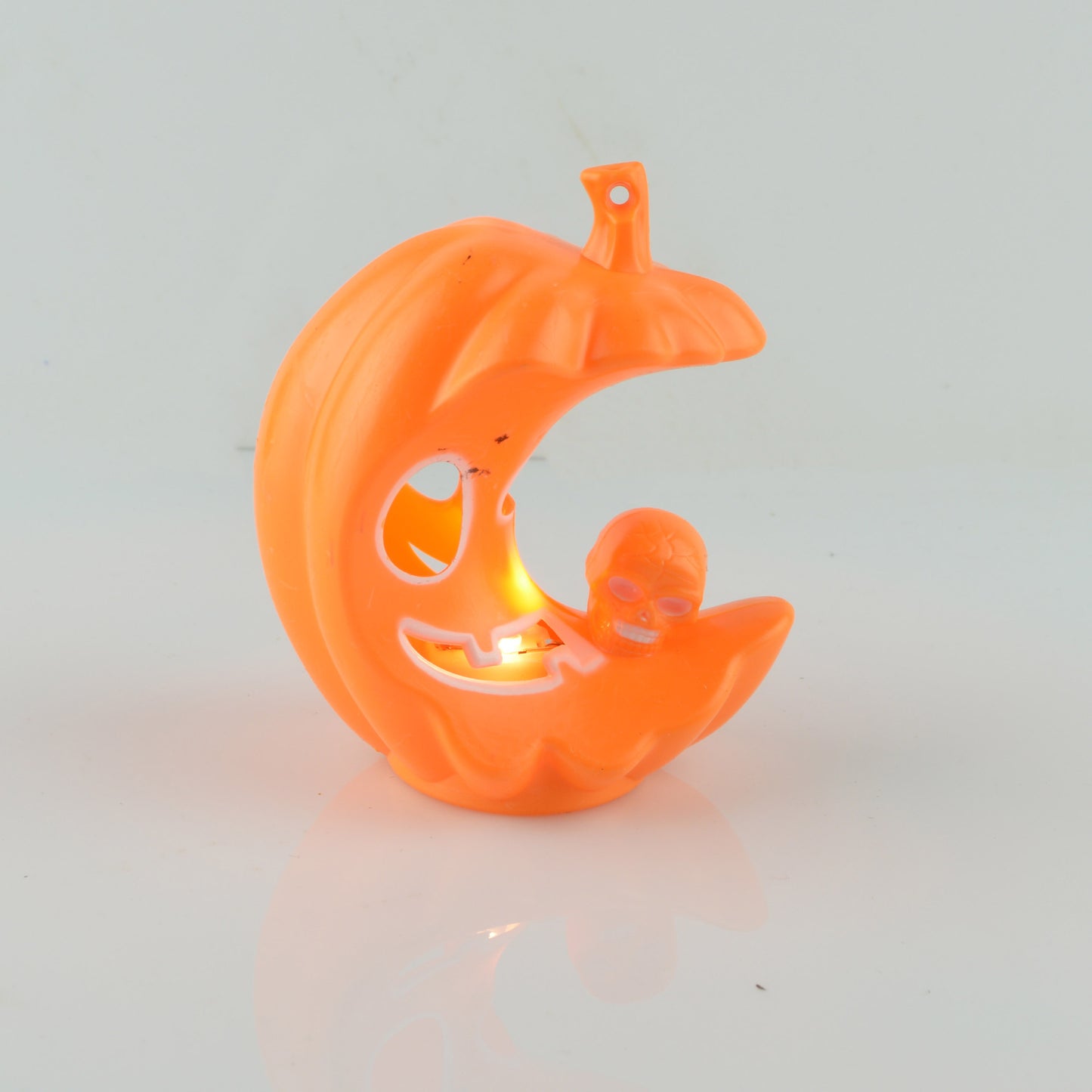 Orange, crescent-shaped pumpkin decoration with a carved face and a small skull. It emits an inner glow, creating a spooky Halloween ambiance.
