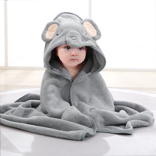 Baby wrapped in a soft, gray elephant-themed hooded blanket, sitting on the floor. Light streams in from a large window in the background.