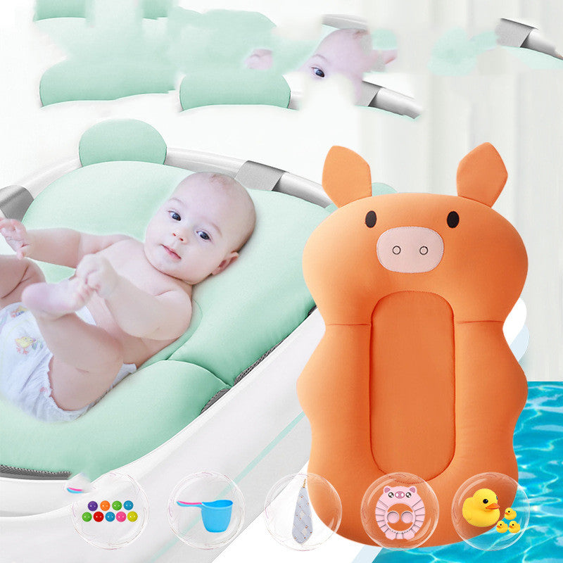 A baby lies on a soft, light green cushion, surrounded by baby products including an orange pig-shaped pillow, a rubber duck, bath scoop, and colorful toy balls.