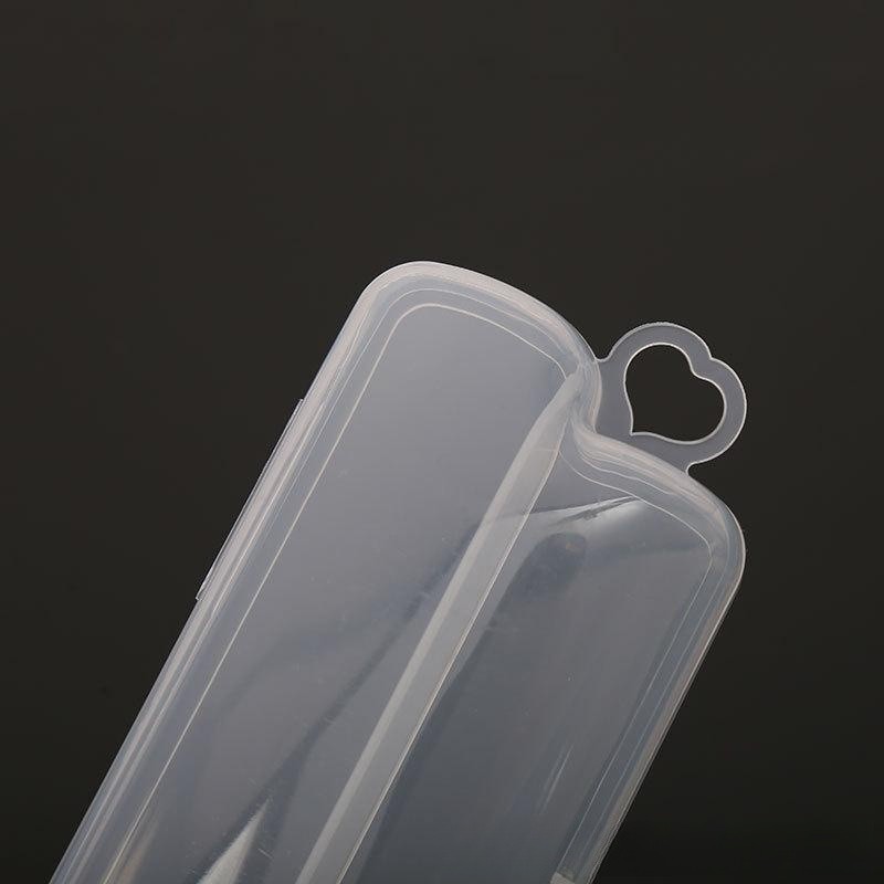 Close-up of a transparent plastic container with a heart-shaped tab on the lid against a dark background. The container is slightly tilted, showing its elongated shape and smooth surface.
