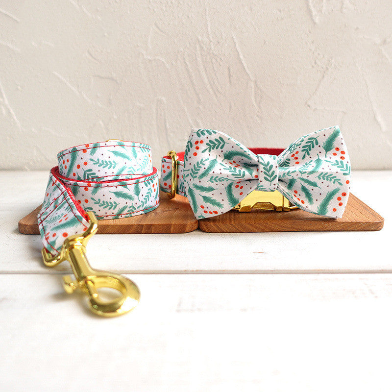 Festive pet leash and bow tie with green leaf and red berry pattern, displayed on a wooden board. Features a gold clasp and is set against a light textured background.