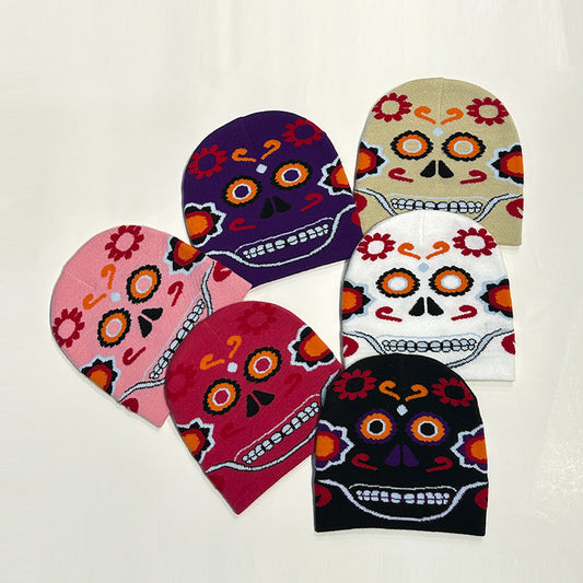 Six colorful beanies with skull designs, featuring vibrant patterns and flowers, arranged in a circle. Colors include purple, beige, pink, red, white, and black.