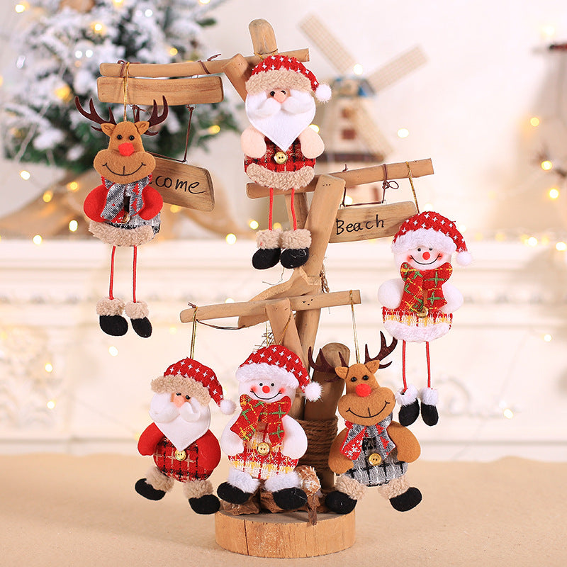 Festive Christmas decorations featuring plush Santa, snowman, and reindeer figures hang on a wooden tree. Fairy lights and a snowy background add a cozy holiday feel.