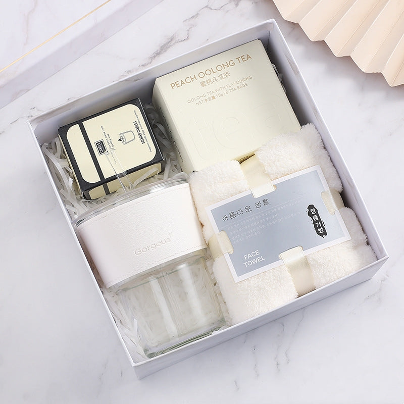 Gift box with peach oolong tea, a face towel, a glass cup with a white sleeve, and a small box of scented tea lights, set on a marble surface.