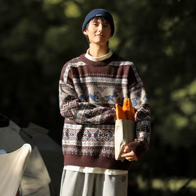 A person in a patterned sweater and blue beanie holds a paper bag with baguettes. They are outdoors, standing in front of a tent and chair with trees in the background.