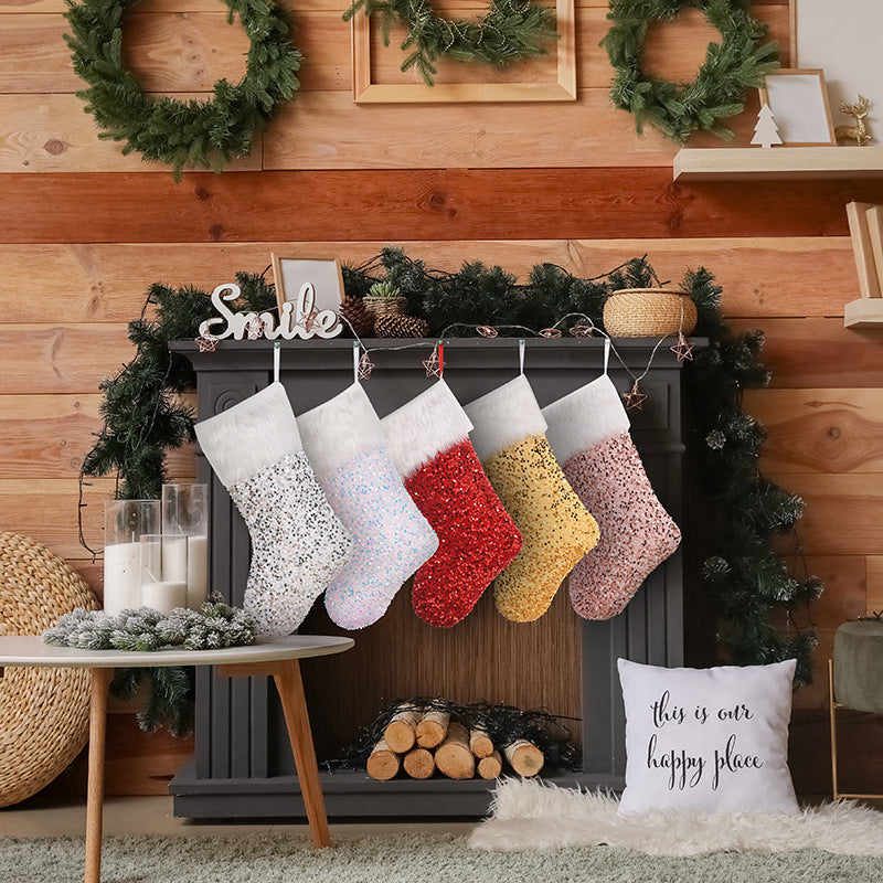 Festive fireplace with four sequined stockings in white, blue, red, and gold. Two green wreaths and garland adorn the mantle. A "Smile" sign and candles add a cozy touch.