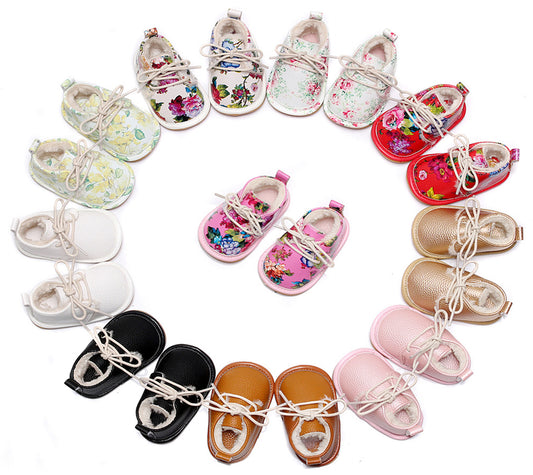 Circle of baby shoes with floral, plain, and metallic designs in various colors including black, brown, white, pink, and red, displayed on a white background.