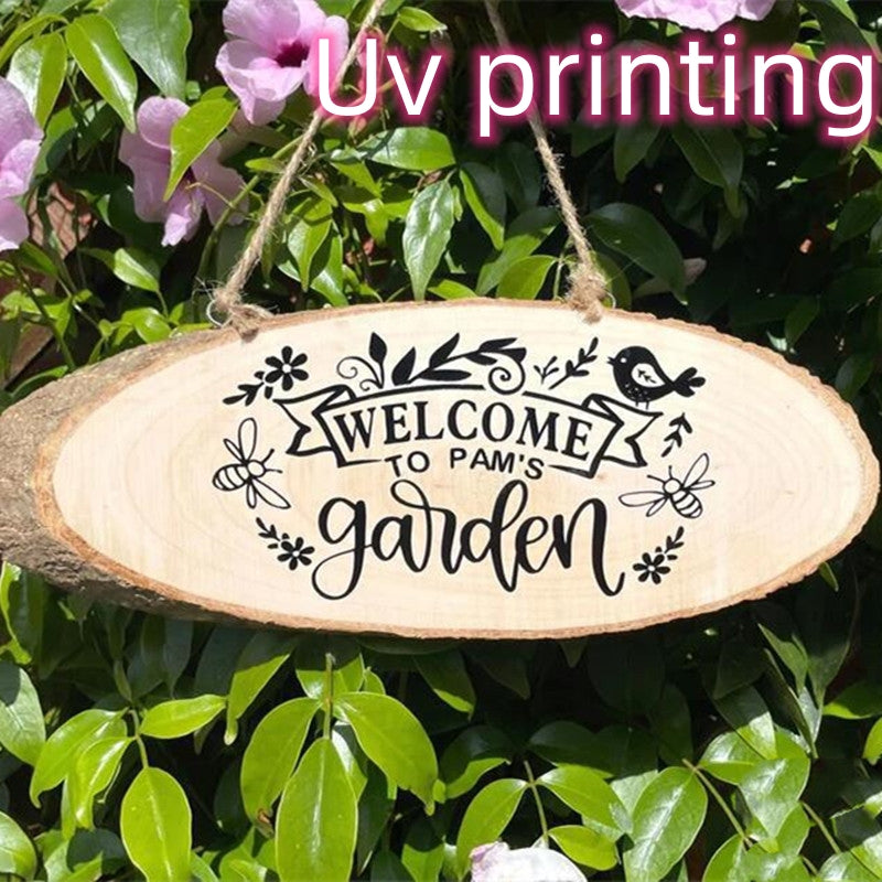 Wooden sign reading "Welcome to Pam's Garden" with floral and bird design, hangs on a rope among green leaves and pink flowers. Text overlay: "Uv printing".