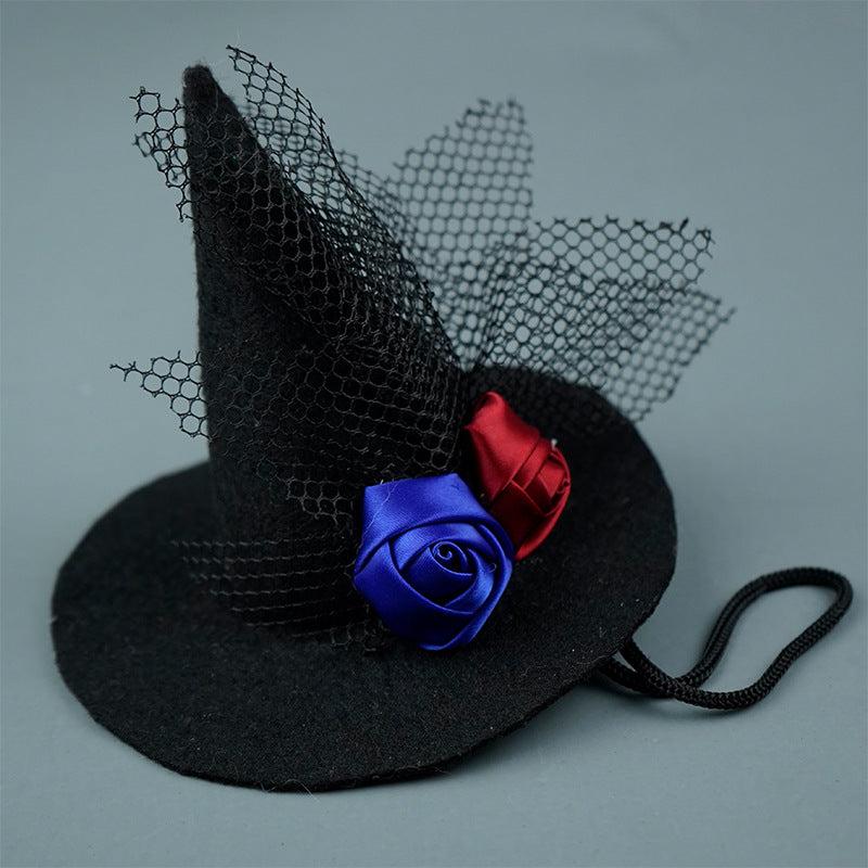 A small black witch hat adorned with black mesh and two satin roses, one blue and one red, on a gray background.