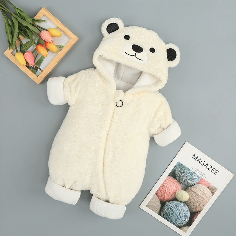 A cream-colored baby jumpsuit shaped like a bear, with a hood featuring ears and a cute face, lies next to colorful tulips in a wooden frame and a knitting magazine.