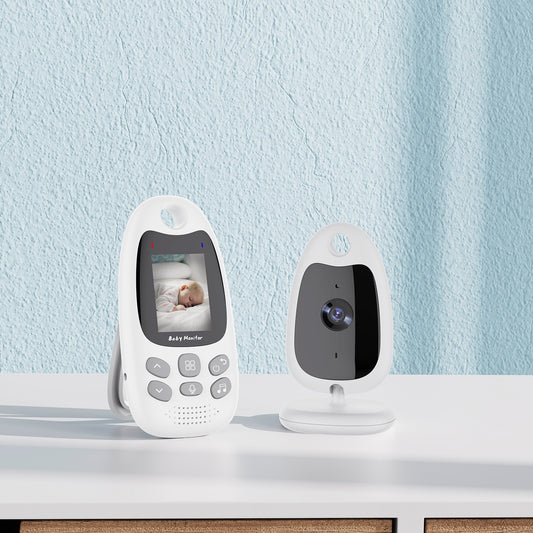 White baby monitor on a table with a camera and a screen showing a sleeping baby. The wall behind is light blue, and the design is sleek and modern.