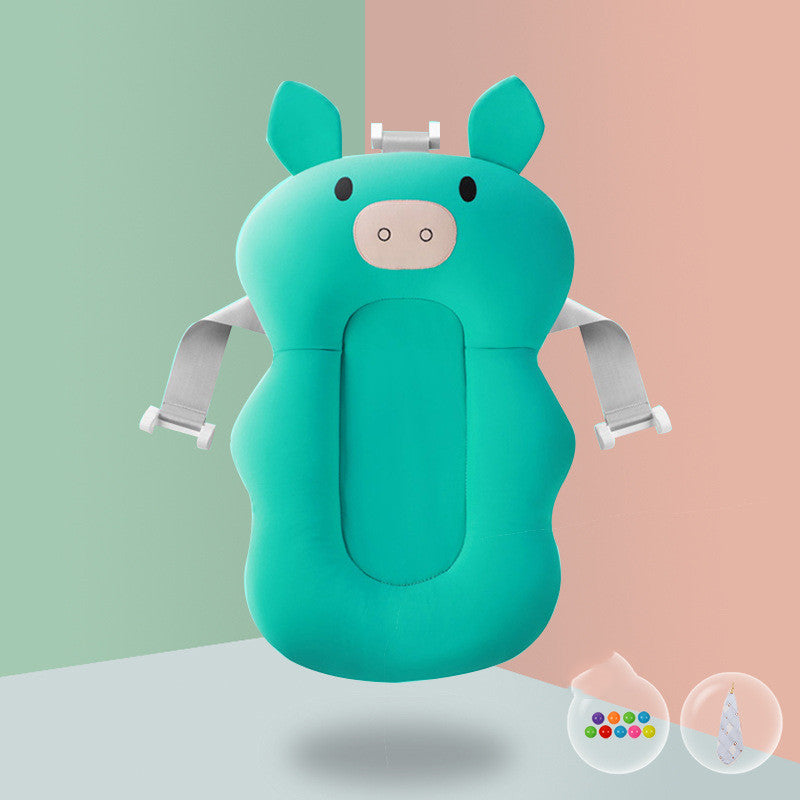 A teal infant bath seat shaped like a cartoon animal with ears and nose, featuring adjustable straps. Two small containers with colorful balls and a striped cone are nearby.