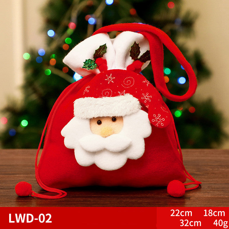 Red fabric Santa gift bag with a fluffy beard and hat, embellished with holly leaves. Set on a table with a blurred background of a Christmas tree and lights. Dimensions: 22cm x 18cm.
