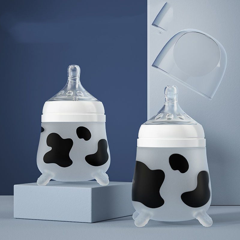 Two baby bottles with cow pattern designs are displayed against a blue background. One bottle is on a raised platform, and a transparent lid is shown floating above.