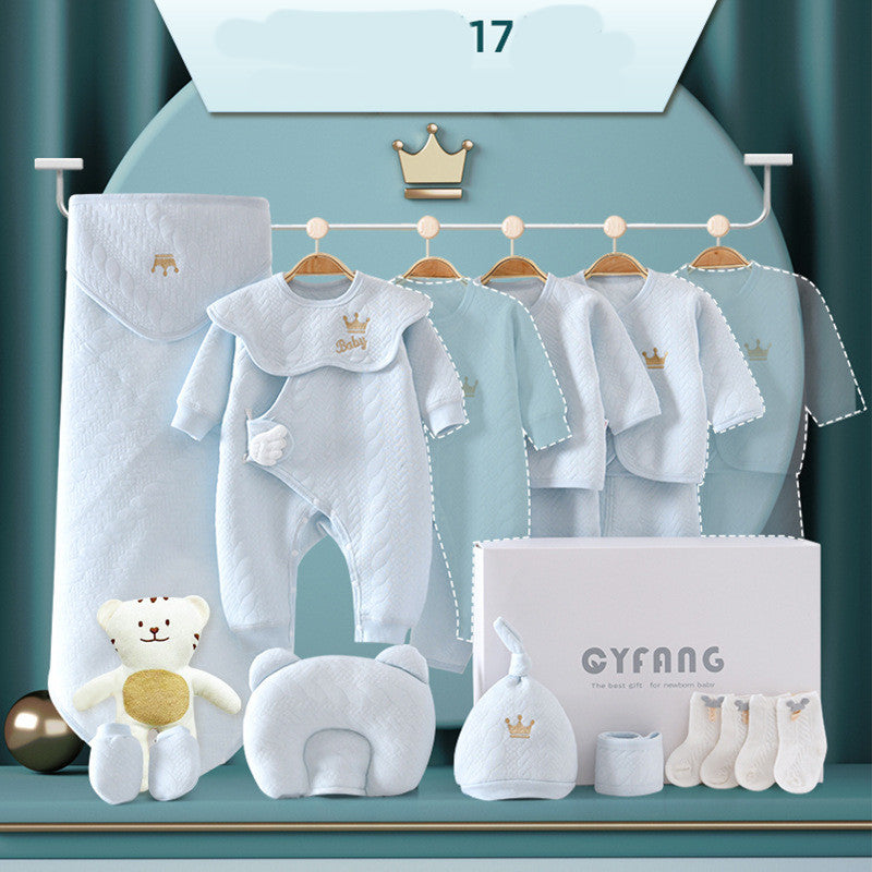 A baby gift set in pastel blue includes clothing, a hat, booties, a pillow, a blanket, and a plush bear. Items feature crown motifs and "Baby" embroidery, displayed with a gift box.