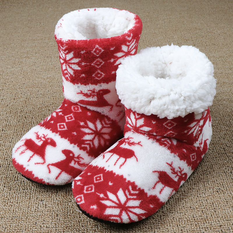 Fuzzy red and white holiday slippers with reindeer and snowflake patterns, placed on a beige carpet.