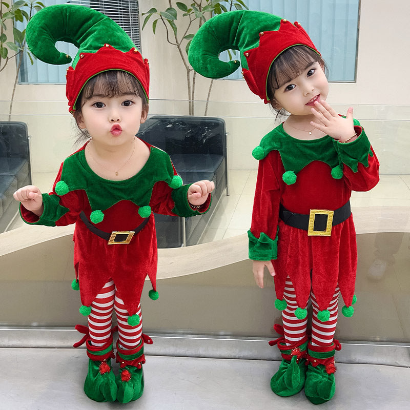 Two young children dressed as festive elves in red and green outfits with striped leggings, pointy hats, and elf shoes, posing indoors in front of a mirror.