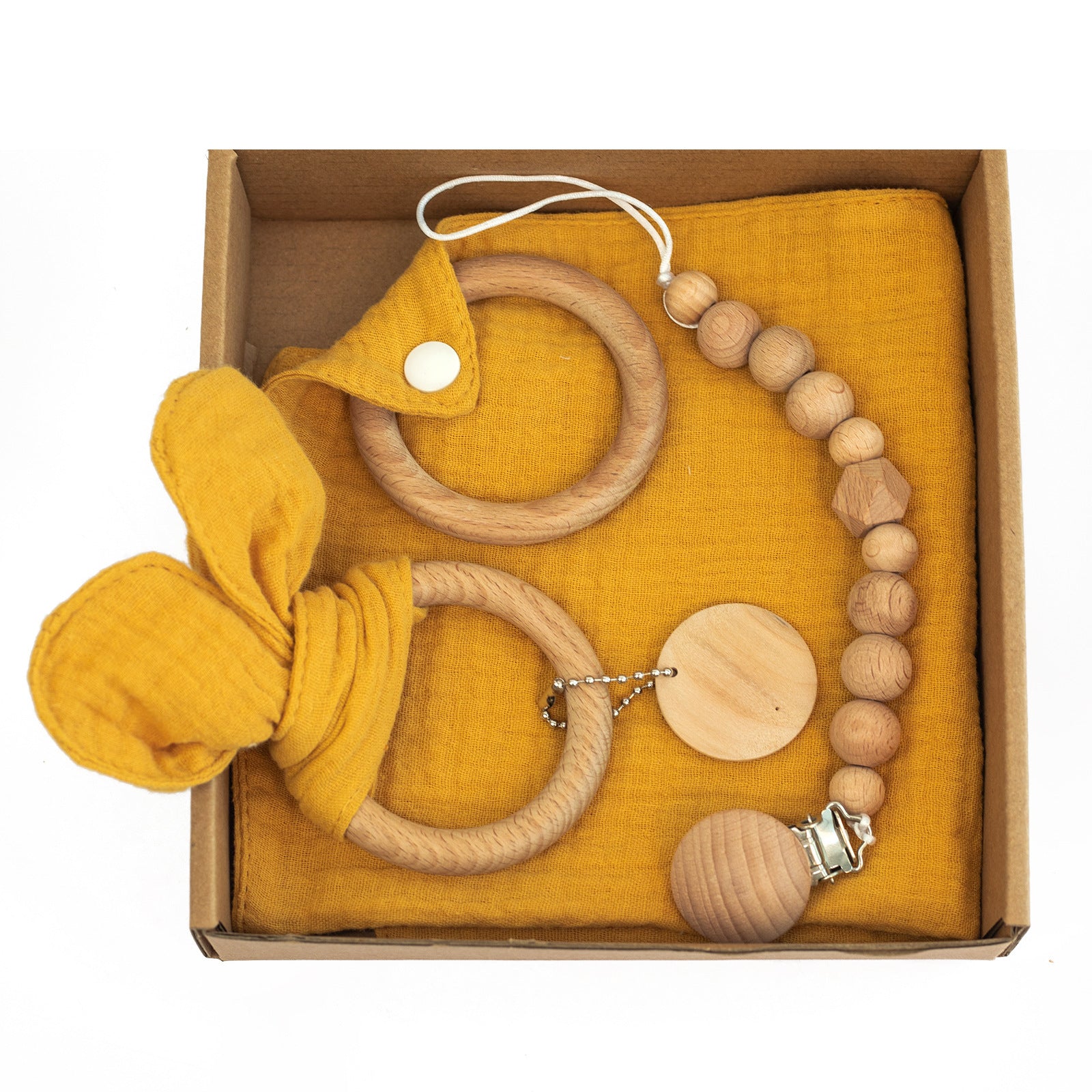 Natural baby gift set in a box with wooden rings, a beaded pacifier clip, and a mustard yellow cloth with a knot.