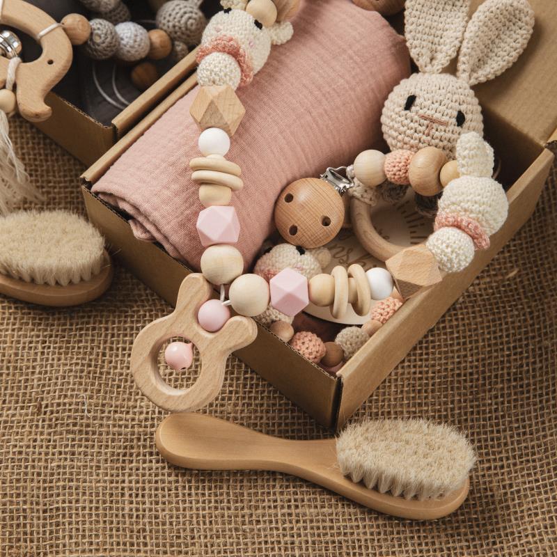 A cozy gift box with wooden baby toys and a crocheted bunny, set on burlap. Includes a teether, pacifier clip with pastel beads, and a soft baby hairbrush.