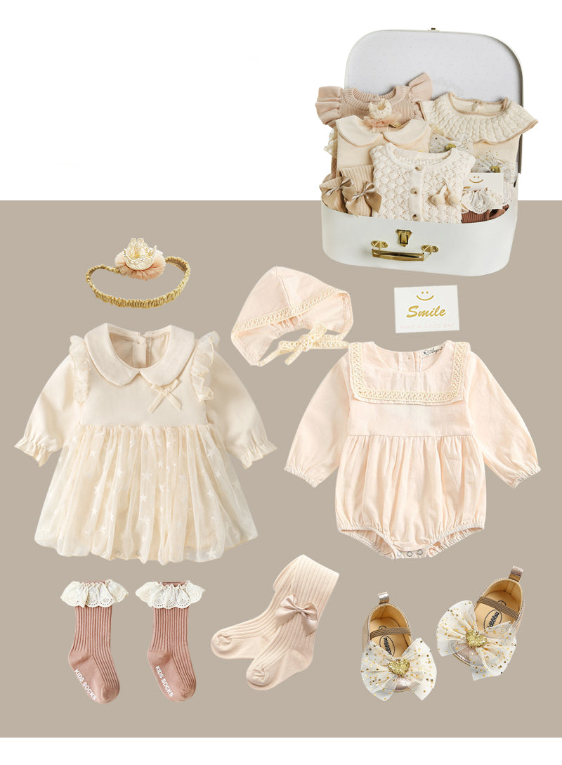 A collection of baby clothes in pastel shades, featuring dresses, rompers, socks, shoes, and hair accessories. They are displayed with a white suitcase, conveying a delicate, elegant style.