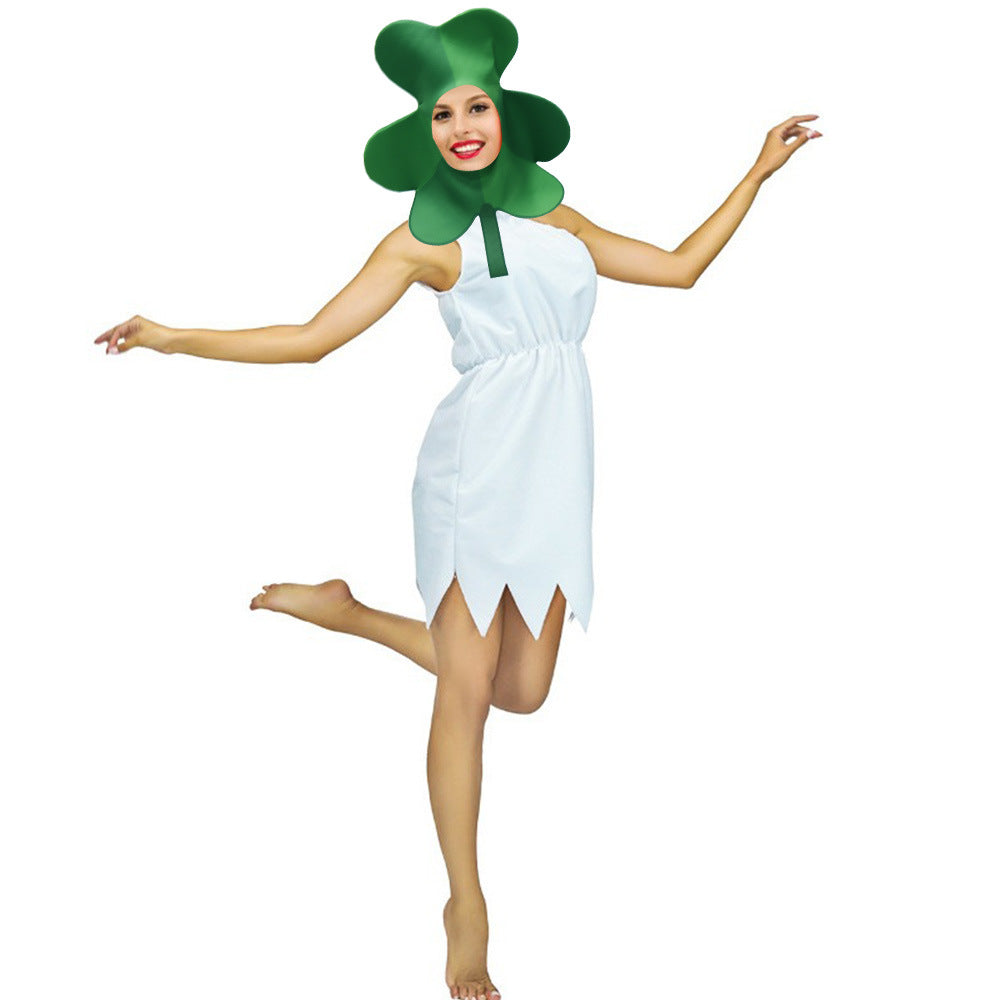 Smiling person in a green clover hat and a white dress, playfully posing with one leg lifted and arms outstretched against a plain white background.